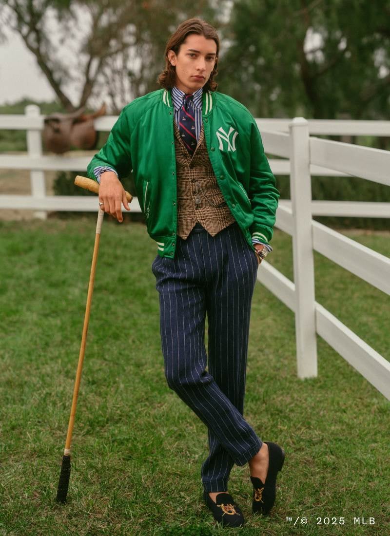 Man on lawn wears green Yankees baseball jacket and navy pinstripe trousers.