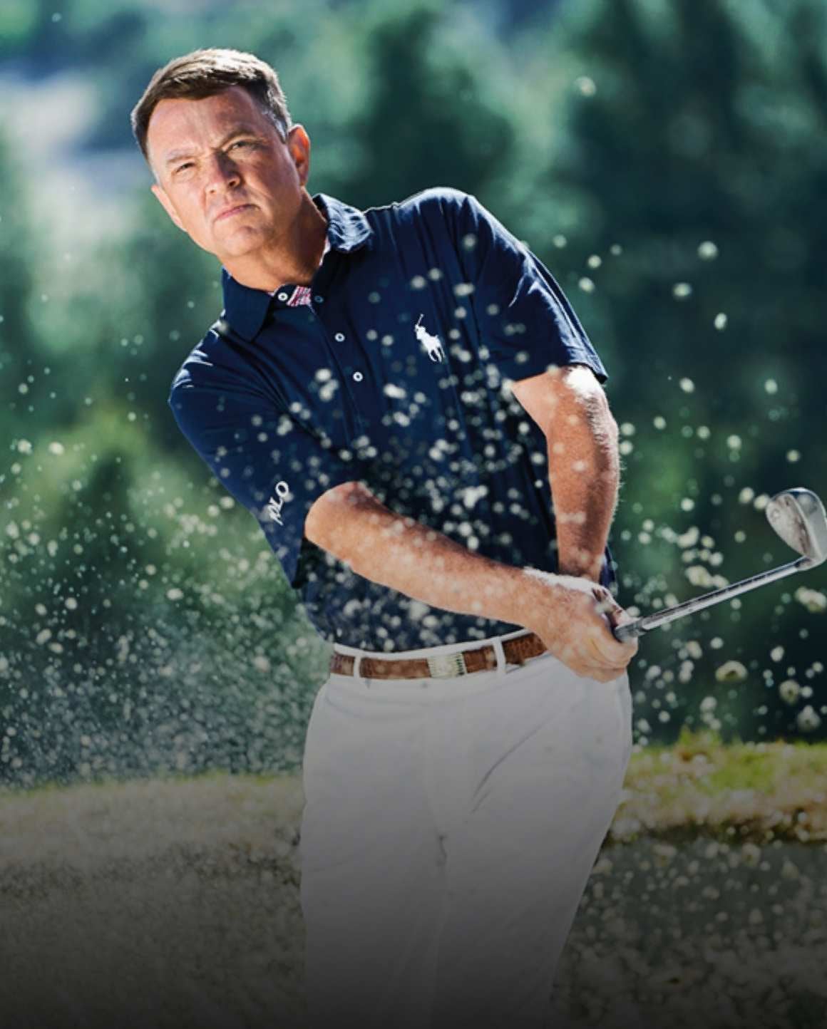 Photo of Davis Love III swinging golf club in navy Polo and white pants.