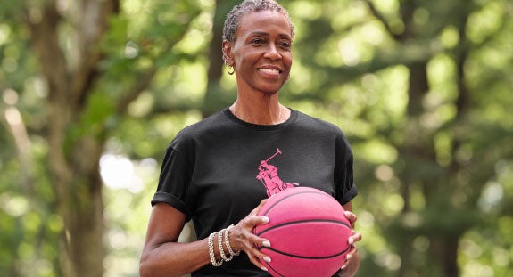 Photograph of woman in black Pink Pony tee holding pink basketball.