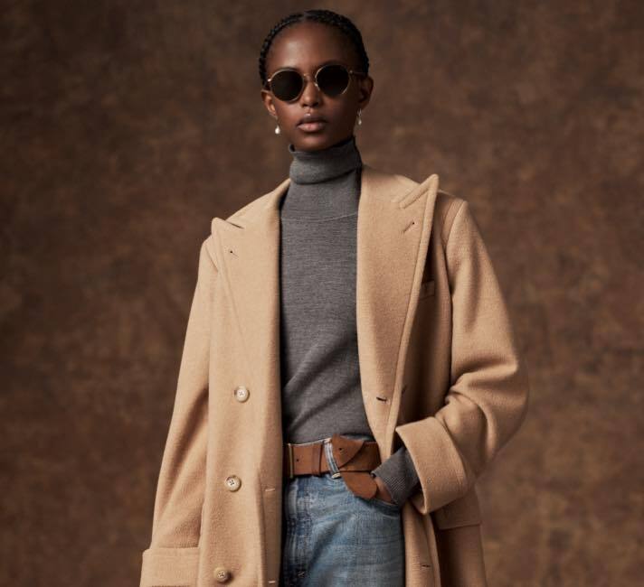 Woman wears camel wool coat over grey turtleneck.